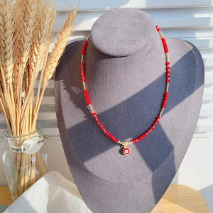 Detailopname van een rode kristallen kralenketting met gouden accenten en Evil Eye hanger