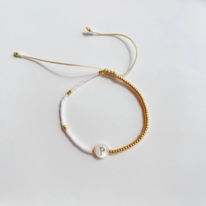 Detail van verstelbare kralenarmband met gouden accenten en schelphanger letter P