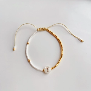 Detail van een handgemaakte kralenarmband met witte kralen en gouden letter T bedeltje