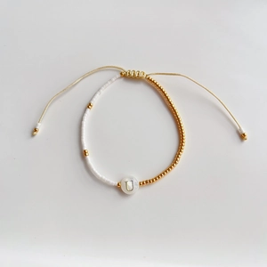 Detail van verstelbare kralenarmband met schelphanger letter U en wit-gouden kralen