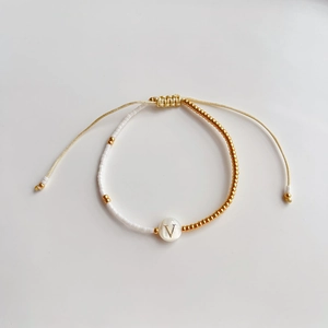 Detailopname van een handgemaakte kralenarmband met witte en gouden kralen en de letter V