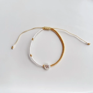Detail van handgemaakte kralenarmband met witte en gouden TOHO-kralen en letter W bedeltje