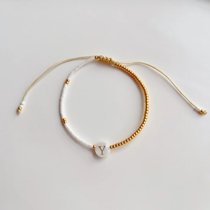 Detail van verstelbare goudkleurige kralenarmband met letter Y bedel en witte vierkante kralen
