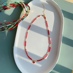 Detail van rode kralenketting met hartvormige hanger op een wit keramisch bord bij daglicht