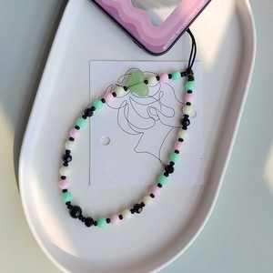 Handmade beaded phone strap with pastel beads and a heart charm on a white tray
