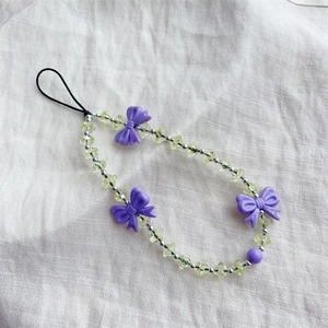 Beaded phone charm with light green crystals and purple 3D bows on beige linen fabric