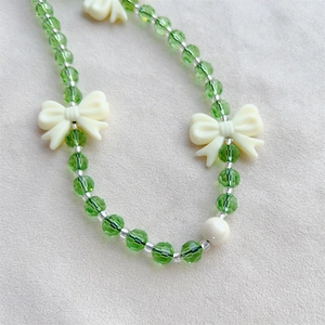 Summer green crystal beaded phone strap with cream bow accessory on beige fabric