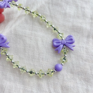 Handmade beaded phone strap with yellow stars and purple bows on a white fabric background