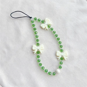 Green crystal bead phone charm with cream bows and black cord on soft fabric