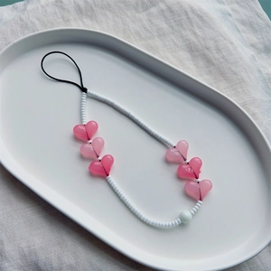 Dragonne de téléphone perlée avec perles blanches et cœurs en acrylique rose sur plateau