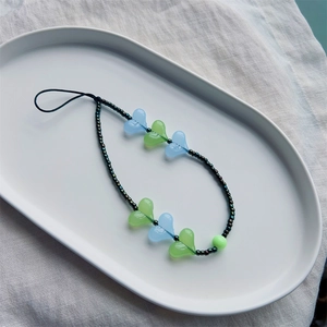 Dragonne de téléphone faite main avec cœurs acryliques et perles sur assiette blanche