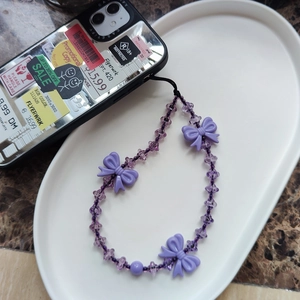 Purple beaded phone strap with butterfly charms displayed on a white decorative tray