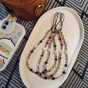 Set of four colorful crystal and pearl beaded phone wrist straps on a white tray