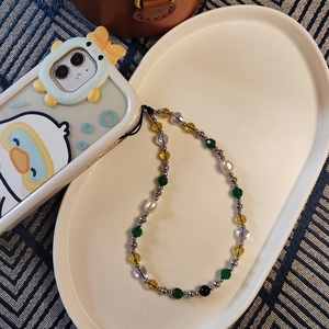 Handmade beaded phone strap with green and yellow crystals on a ceramic tray
