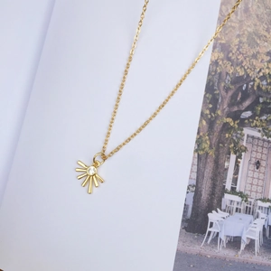 Minimalist 18K gold sunburst pendant necklace with a center zircon on magazine background