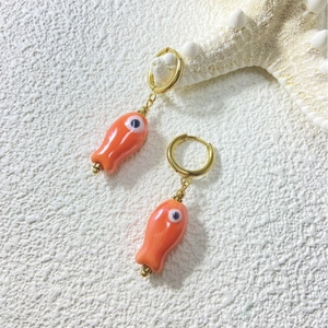 Cute orange ceramic fish earrings with golden hoops and devil eye design on white background
