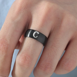 Detalle de un anillo de acero inoxidable negro mate con la letra C grabada en plata