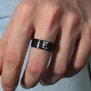 Primer plano de un anillo de acero negro mate con la letra E grabada en un dedo