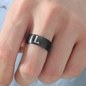 Detalle de anillo de acero inoxidable negro mate con letra L blanca y textura cepillada