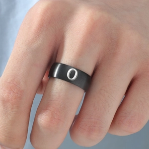 Detalle de anillo de acero inoxidable negro mate con la letra O blanca grabada en el dedo