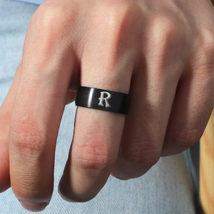 Detalle de un anillo de acero inoxidable negro mate con la letra R plateada en la mano