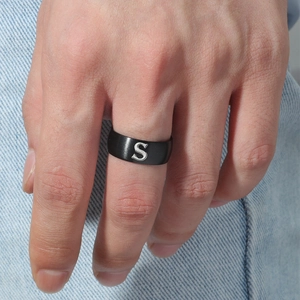 Detalle de un anillo de acero inoxidable negro mate con la letra S grabada en un modelo