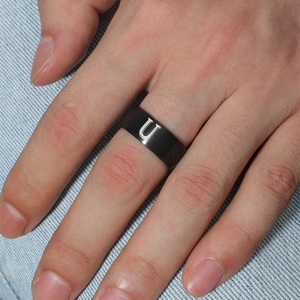 Detalle de anillo de acero inoxidable negro mate con letra U blanca en mano de hombre