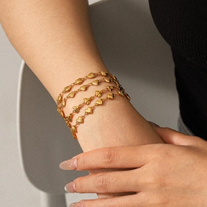 Close-up of a layered golden heart and shell charm bracelet worn on a woman's wrist