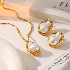 Dettaglio della collana a catena dorata e orecchini di perle barocche su sfondo caldo tramonto