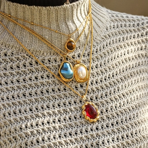Colliers dorés vintage superposés avec pendentifs en pierre sur un pull femme