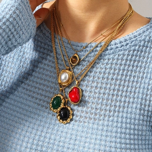 Détail de colliers dorés superposés avec pendentifs géométriques aux pierres colorées