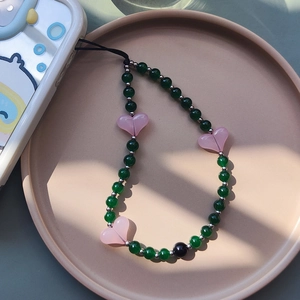 Detail of green beaded phone charm with pink resin hearts and silver spacers on ceramic tray