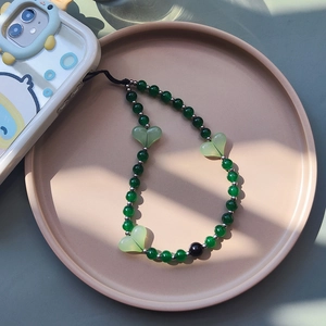 Green resin heart beaded phone charm strap on a white phone case over ceramic plate