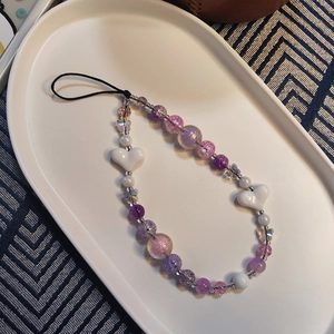 Handmade amethyst purple beaded phone charm with white heart accents on a stylish tray
