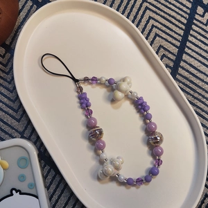 Detail of beaded phone strap featuring purple bears and white cloud beads in a tray