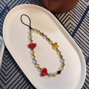 Handmade beaded phone strap with yellow duck and red heart charms on a white tray