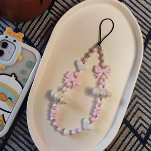 Dettaglio del laccetto per telefono con fiocco rosa, cuore bianco e charms orso