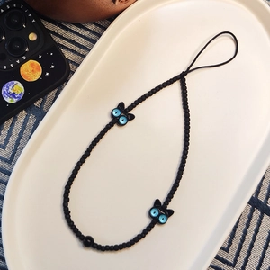 Détail de bijou de téléphone chat noir avec yeux bleus et perles noires mates