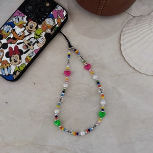 Colorful handmade seed bead phone charm with heart pendants on marble surface