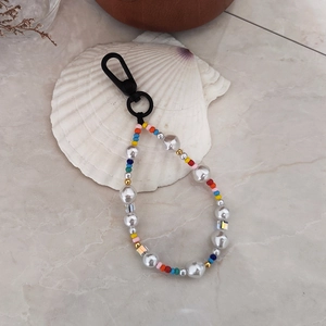 Detailed close-up of colorful baroque pearl and rainbow bead keychain on a shell background