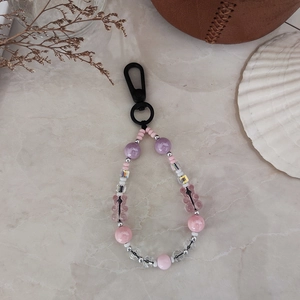 Detail of beaded bear keychain with pink and purple heart charms on marble background