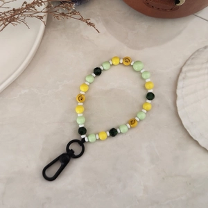 Handmade beaded lime green smiley face keychain with black lobster clasp on marble surface