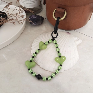 Handmade green heart and striped bead keychain charm hanging on a brown leather bag