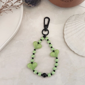 Detailed view of green striped acrylic beads and heart charms on a black metal keychain