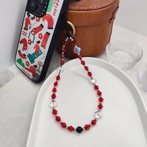Red beaded phone wrist strap with crystal clover charms on elegant ceramic dish