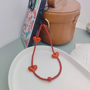 Handmade red beaded phone charm strap with cherry bomb heart accents in a ceramic tray