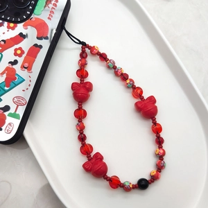 Red beaded phone charm with crystal beads and heart bow pendants on white ceramic