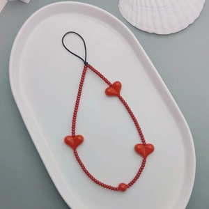 Red heart beaded phone strap on a white tray with shell detail in high quality macro view