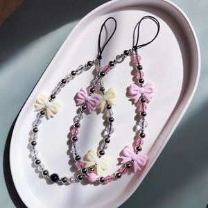 Sweet acrylic beaded phone straps with bow pendants and metallic beads in a ceramic dish