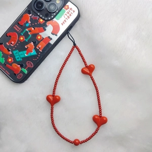 Detail of red heart beaded phone strap with acrylic charms on white faux fur background